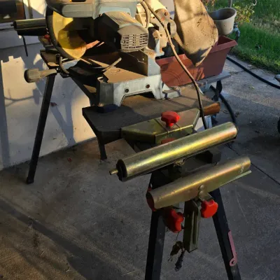 Sale Photo Thumbnail #96: Ryobi compound miter saw mounted on a portable saw stand with roller extensions, showing visible wear and dust from prior outdoor use.