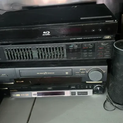Sale Photo Thumbnail #19: Stack of home electronics including a Sony Blu-ray player, Akai graphic equalizer, Toshiba VCR, and Panasonic DVD player alongside a smart speaker.