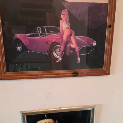 Sale Photo Thumbnail #106: Pair of framed wall art pieces including a vintage 1980s pin-up poster with a pink sports car in a wooden frame and a Grolsch Lager Beer mirror featuring classical portraits.