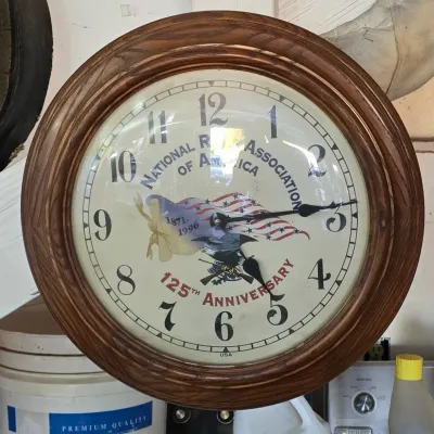 Sale Photo Thumbnail #103: National Rifle Association 125th Anniversary wall clock featuring a wooden frame, bald eagle and American flag face design, circa 1996.