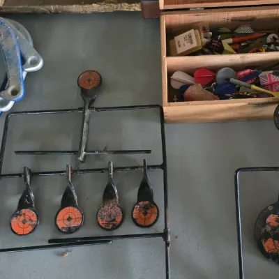 Sale Photo Thumbnail #22: Collection of outdoor game accessories including metal spinning target stands, blue and silver pitching horseshoes, and a wooden box filled with dart supplies.