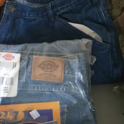Sale Photo Thumbnail #24: Stack of men's pants including new-in-packaging Dickies work jeans alongside blue jeans and camouflage cargo pants.