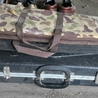Sale Photo Thumbnail #25: Stack of long gun carrying cases, including a camouflage soft case, a black fabric soft case, and a black molded hard case.