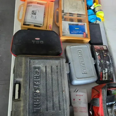 Sale Photo Thumbnail #63: Collection of mixed power tools, hard cases, and hardware accessories including Craftsman, Dremel, Ryobi, and Black & Decker items displayed on a table.