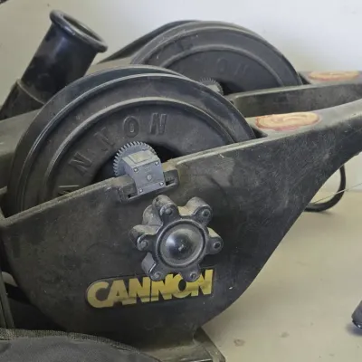 Sale Photo Thumbnail #81: Pair of vintage Cannon downriggers featuring black composite housings, rod holders, and manual spool knobs.