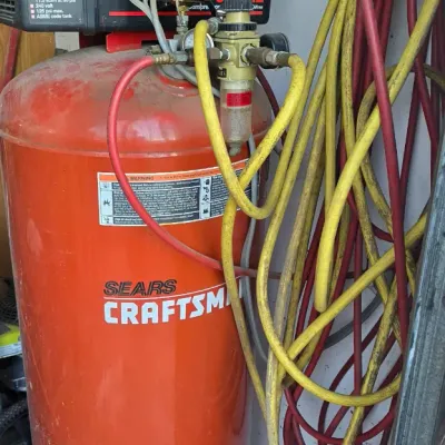 Sale Photo Thumbnail #69: Sears Craftsman 60-gallon vertical air compressor with attached air filter regulator and hanging pneumatic hoses.