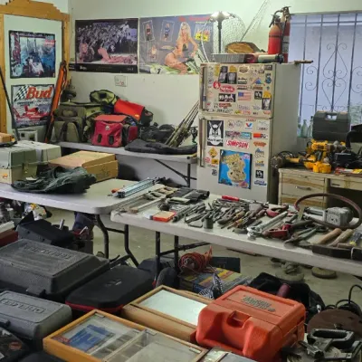 Sale Photo Thumbnail #3: Workshop and garage setup featuring folding tables laid out with various hand tools, power tools, tackle boxes, and storage cases.