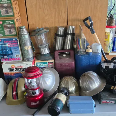 Sale Photo Thumbnail #57: Collection of vintage outdoor camping gear and hard hats, including Coleman stoves, lanterns, thermoses, and Mr. Heater equipment.