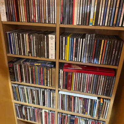Large collection of music CDs in jewel cases, organized across multiple shelves in a light-colored wooden bookcase.