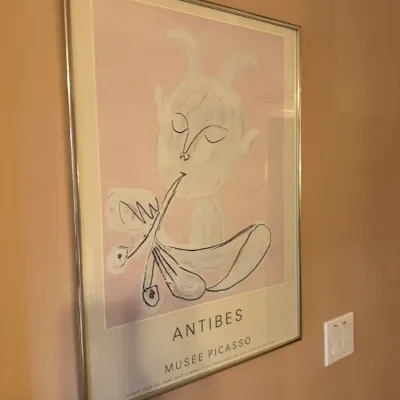 Framed exhibition poster for Musée Picasso in Antibes, featuring a pink and white faun motif in a thin metal frame.
