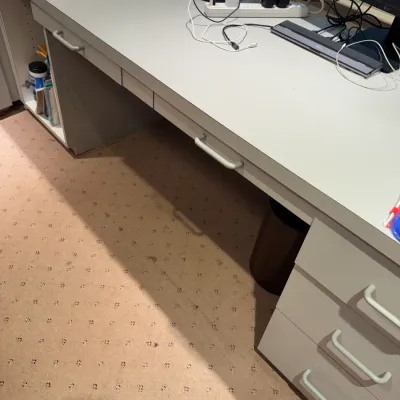 Large white office desk featuring built-in side drawers, side storage cabinets, and center drawers, paired with dual computer monitors...