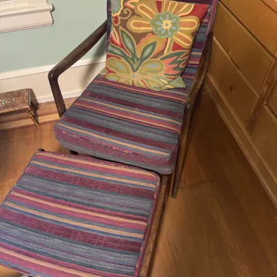 Mid-century modern wooden armchair and matching ottoman with striped fabric upholstery and a floral throw pillow.