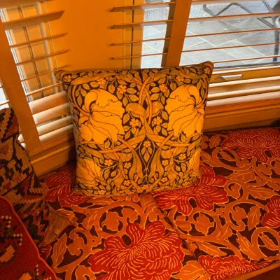 Square accent pillow featuring a William Morris-style Art Nouveau botanical pattern, resting on a floral window seat cushion.