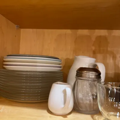 Collection of modern kitchenware, including stackable ceramic plates and bowls, white creamer pitchers, a glass sugar shaker with metal...