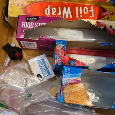 Wooden kitchen drawer filled with household food storage supplies including Glad Cling 'N Seal, ShopRite Foil Wrap, zip-top bags,...