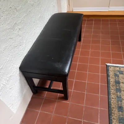 Black faux leather upholstered entryway bench with wooden base, showing minor wear on the seat.