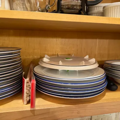 Stacks of ceramic dinnerware with blue rims stored on a wooden cabinet shelf alongside a plastic turntable organizer.