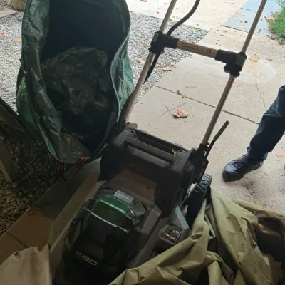 EGO Power+ cordless electric lawn mower shown outdoors next to a large pop-up garden waste bag.