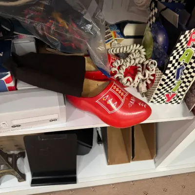 Pair of red painted Dutch wooden clog shoes with hand-painted white folk details, stored on a shelf alongside various miscellaneous...