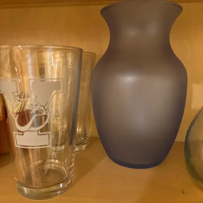 Frosted purple glass vase alongside etched drinking glasses displayed on a wooden shelf.
