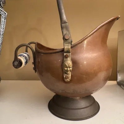 Vintage copper and brass helmet-style coal scuttle bucket featuring embossed face detailing on the handle mounts and a blue-and-white...
