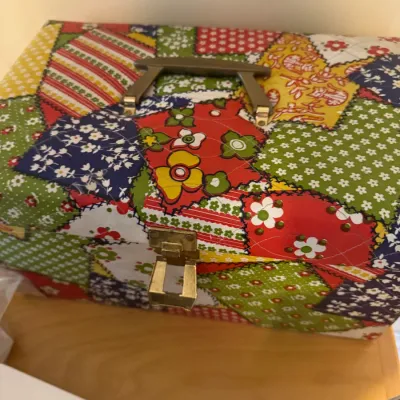 Vintage 1970s quilted fabric sewing box with a colorful patchwork floral print, plastic handle, and brass latch.