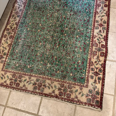 Hand-knotted vintage area rug featuring a teal green field with a dense floral pattern and a cream floral border.