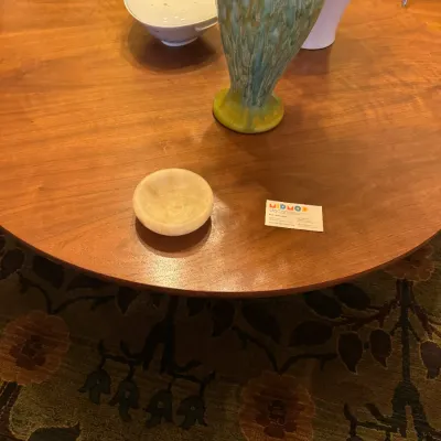 Mid-century modern round wooden coffee table displaying a green glazed ceramic vase, small stone dish, and white porcelain covered bowl.