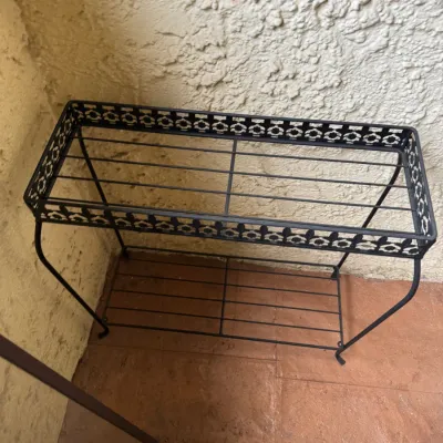 Black wrought iron two-tier plant stand featuring decorative filigree trim and slat shelves.