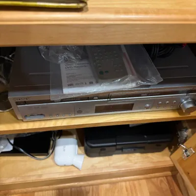 Sony silver VCR and DVD recorder combo unit with manual and remote control included on a wooden shelf.