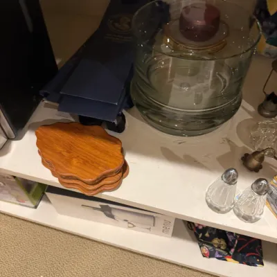 Collection of household items on a shelf, including a set of shaped wooden coasters, clear glass bowls, and cut crystal salt and pepper...