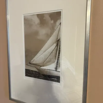 Framed black and white nautical photograph of a sailboat at sea, featuring a wide white mat and a silver-tone metal frame.