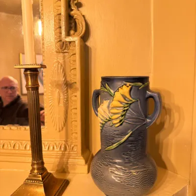Roseville Pottery Freesia pattern blue double-handled vase displayed on a shelf alongside a classical brass candlestick.