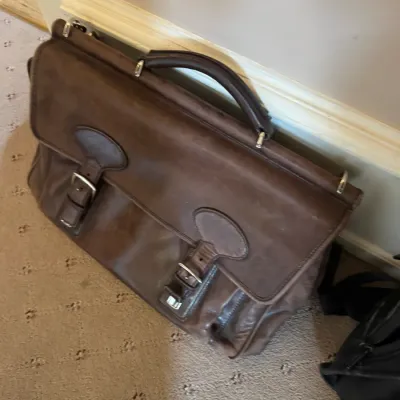 Vintage dark brown leather briefcase featuring twin front buckle straps and a top carrying handle.
