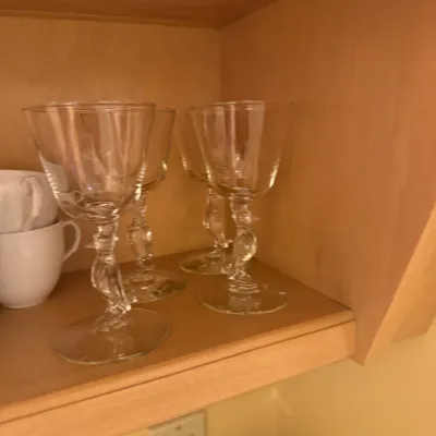 Set of clear wine stemware featuring sculpted bird figurine stems, displayed inside a wooden cabinet.