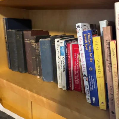 Collection of books on a wooden shelf, including Jewish themed literature, prayer books, and a Holy Bible.