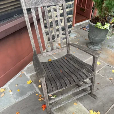Weathered wooden porch rocking chair featuring a slatted backrest and contoured seat.