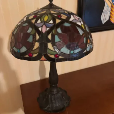 Tiffany-style table lamp with a colorful leaded stained glass dome shade resting on a sculpted dark metal base.