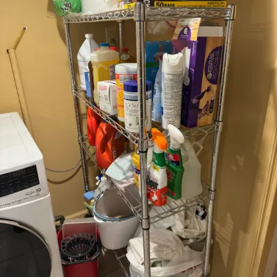 Five-tier chrome wire shelving unit filled with household cleaning supplies, detergent, and trash bags.