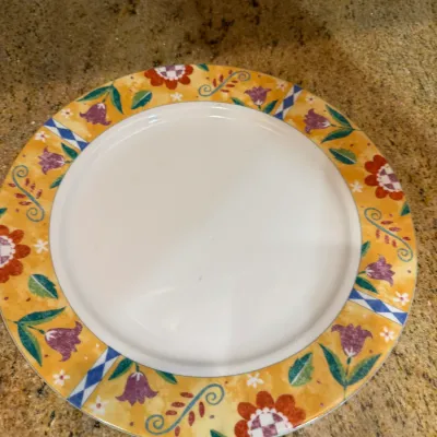 Ceramic dinner plate featuring a colorful rim decorated with red and purple floral patterns and blue accents, resting on a stone countertop.
