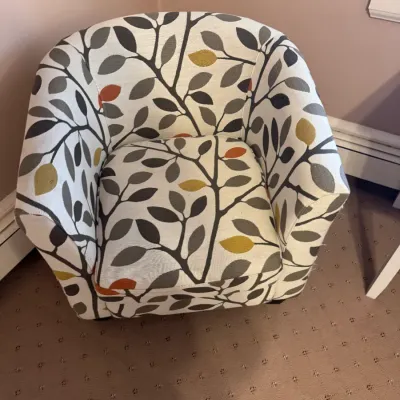 Contemporary barrel armchair upholstered in a botanical leaf pattern fabric with mustard yellow, rust, and gray accents.