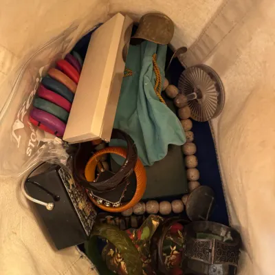 Canvas tote bag filled with assorted vintage fashion accessories, including colorful bangle bracelets, beaded necklaces, and small...