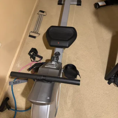 Compact magnetic rowing machine in gray and black casing, shown alongside various fitness accessories.