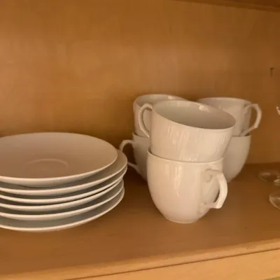Set of modern white ceramic teacups and matching saucers stacked on a wooden shelf.