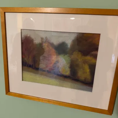 Framed impressionist pastel landscape painting of autumn trees and a field, presented in a light wood frame with a wide white mat.