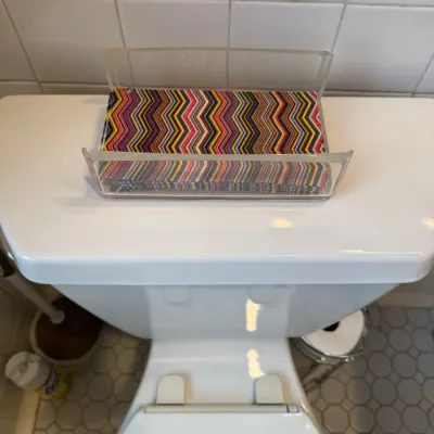 Clear acrylic paper guest towel tray filled with colorful chevron-patterned disposable hand towels, resting atop a toilet tank.