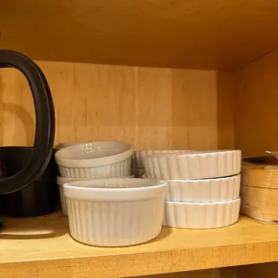 Collection of white ceramic ramekins and shallow baking dishes, stacked on a wooden shelf.