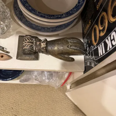 Vintage brass hand-shaped door knocker featuring an ornate cuff detail, shown alongside a stack of blue and white rimmed ceramic bowls.