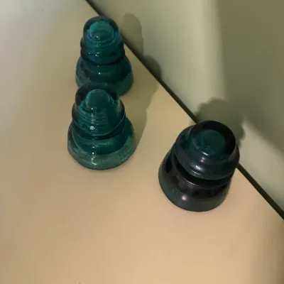 Trio of antique glass telegraph insulators, including two in aqua blue and one in dark green, displayed on a flat surface.
