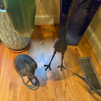 Set of dark metal or bronze heron and crane bird statues displayed on a hardwood floor next to potted plants.
